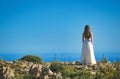 A bride in a white wedding dress standing on a cliff edge looking out to sea