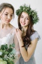 Bride in white wedding dress standing with her smiling bridesmaid in pine wreath and blue dress