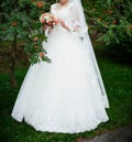 The bride in a white wedding dress stands near the rowan trees with a beautiful bouquet in her hands Royalty Free Stock Photo