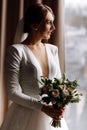 Bride in white wedding luxury dress with bouquet of flowers near the window in hotel room. happy beautiful young woman with Royalty Free Stock Photo