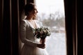 bride in white wedding luxury dress with bouquet of flowers near the window in hotel room. happy beautiful young woman Royalty Free Stock Photo