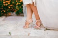 Bride& x27;s legs in stylish sandals with crystals with high heels peek out from under the wedding dress, close-up