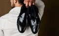Bridegroom holding elegant black shoes behind his back over brown background Royalty Free Stock Photo