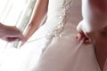 Bridesmaid helping bride fasten buttons on corset and getting her dress Royalty Free Stock Photo