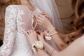 Bridesmaid helping bride fasten corset and getting her dress, preparing bride in morning for the wedding day