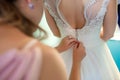 Bridesmaid helping slender bride lacing her wedding white dress, buttoning on delicate lace pattern with fluffy skirt on waist. Royalty Free Stock Photo