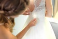 Bridesmaid helping slender bride lacing her wedding white dress, buttoning on delicate lace pattern with fluffy skirt on waist. Royalty Free Stock Photo