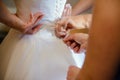 Bridesmaid helping slender bride lacing her wedding white dress, buttoning on delicate lace pattern with fluffy skirt on waist. Royalty Free Stock Photo