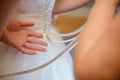 Bridesmaid helping slender bride lacing her wedding white dress, buttoning on delicate lace pattern with fluffy skirt on waist. Royalty Free Stock Photo