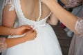 Bridesmaid helping slender bride lacing her wedding white dress, buttoning on delicate lace pattern with fluffy skirt on waist. Royalty Free Stock Photo