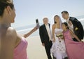 Bridesmaid photographing newly weds with family on beach