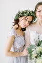 Bridesmaid in pine wreath and blue dress holding her hand on the arm of bride in white wedding dress standing
