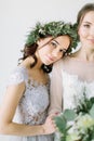 Bridesmaid in pine wreath and blue dress holding her hand on the arm of bride in white wedding dress standing