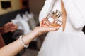 A bridesmaid`s hand holding a bottle with perfume on bride in white dress background. Morning of the bride in the house, hands Royalty Free Stock Photo