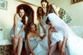 Bridesmaids help bride to put on shoes while she sits on the sofa