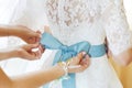 bridesmaids tie a blue bow on the wedding dress. preparation for ceremony  the morning of the bride Royalty Free Stock Photo