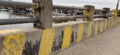 The bridge fence whose paint has started to fade and is damaged and you can see a view of the river below