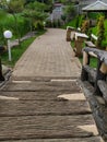 Bridge leads to pathway with green garden and wooden tables and chairs at Kampoeng Banyumili Resto in Semarang