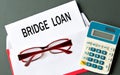 BRIDGE LOAN - words on a white sheet of paper with an envelope, calculator and glasses in the background Royalty Free Stock Photo