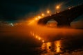 A bridge over an icy river at winter night. the snow-covered bank of the winter river at night, from which steam rises. Royalty Free Stock Photo