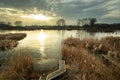 A bridge among reeds on the shore of a frozen lake, the sun setting behind the clouds, evening view Royalty Free Stock Photo