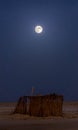 The bridght full moon over the wooden house in the middle of Sahara desert.
