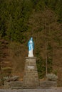 Bright blue and white statue of Lady Mary praying on a brick pedestal