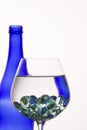 Bright abstraction blue bottle is reflected in a glass with liquid and decorative balls