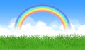 Bright arched rainbow with blue sky, clouds and green grass.