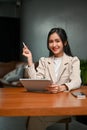 Bright Asian businesswoman at her desk, using tablet, smiling and looking at the camera Royalty Free Stock Photo