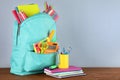 Bright backpack with school stationery on brown wooden table against grey background