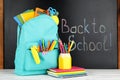 Bright backpack with school stationery on white wooden table near black chalkboard Royalty Free Stock Photo