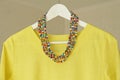 Bright beads of Murano glass hang on the background of a yellow summer dress. Summer jewelry, summer clothes