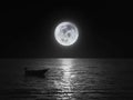 Bright and beautiful dramatic super moon over the ocean with small boat and reflection of bright light in black and white. Image Royalty Free Stock Photo