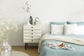 A bright bedroom interior with sage green and white bedding, pillows on bed and a drawer nightstand. Real photo. Royalty Free Stock Photo