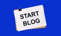 On a bright blue background, an envelope and a sheet of paper with the text START BLOG under the paper clip Royalty Free Stock Photo