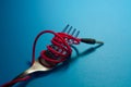 On bright blue background lies fork with wound red cord from headphones as spaghetti. Mobile accessories.