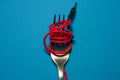 On bright blue background lies fork with wound red cord from headphones as spaghetti. Mobile accessories.