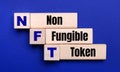 On a bright blue background, light wooden blocks and cubes with the text NFT Non Fungible Token
