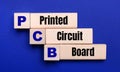 On a bright blue background, light wooden blocks and cubes with the text PCB Printed Circuit Board Royalty Free Stock Photo