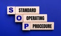 On a bright blue background, light wooden blocks and cubes with the text SOP Standard Operating Procedure Royalty Free Stock Photo
