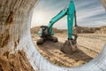 A bright blue excavator operates at a construction site, digging into the earth as the sun sets on the horizon, creating a warm Royalty Free Stock Photo