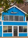 Bright blue house in sunlght decorated with fish on the top. Facade of a colorful house with door and windows Royalty Free Stock Photo