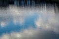 Bright blue January sky, fluffy white clouds and silhouettes of trees reflecting in the calm waters of a city lake