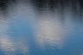 Bright blue January sky, fluffy white clouds and silhouettes of trees reflecting in the calm waters of a city lake