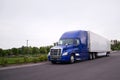 Bright blue big rig semi truck with reefer running on the road