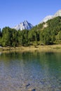 Bright blue mountain lake under blue sky with woods, stones and snow Royalty Free Stock Photo