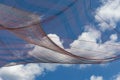 Bright blue sky with clouds, draped pink and blue striped mesh shade cloth foreground, creative copy background