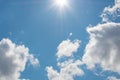 Bright blue sky with sunbeams and fluffy white clouds on a sunny day.