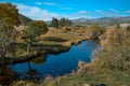 Bright blue winding river flows in grass, bushes, trees among the mountains and sky with clouds. Reflections in clear water. Autum Royalty Free Stock Photo